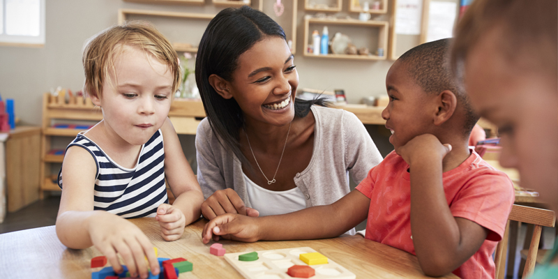 Early Childhood Educator plays at a table with three young children