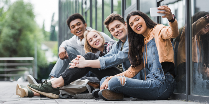 Group of teens sit together and take a selfie on an iphone