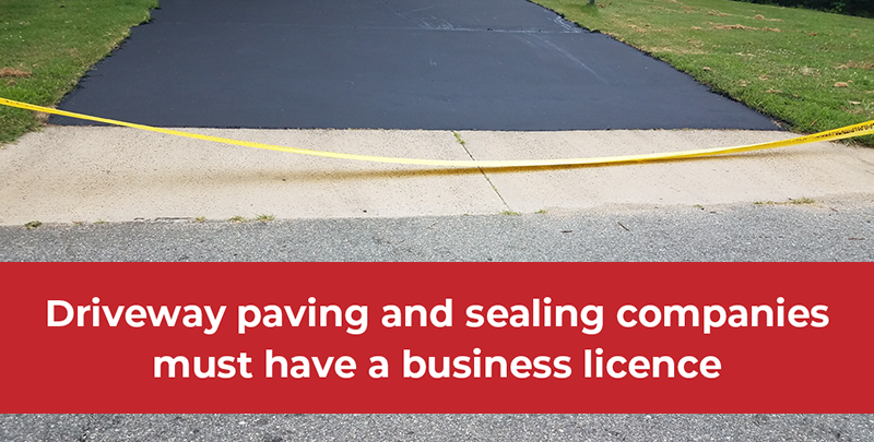 a tight shot of a freshly sealed driveyway with caution tape and text that says driveway paving and sealing companies must have a business licence 