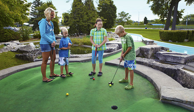 An adult and two children playing mini golf